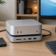 Mac mini on a matching docking stand with front ports, connected monitor, keyboard, and external SSD.